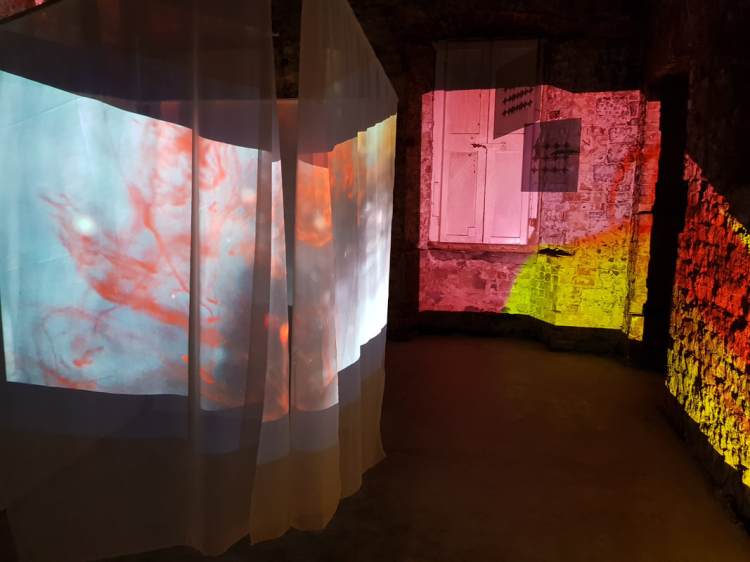 Abstract images are projected onto a stone wall to the right and onto hanging fabric to the left.